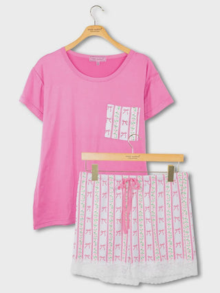 Pink t-shirt and white shorts with pink bows on a hanger against a white background
