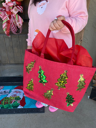 Red bag with green Christmas tree patterns held by a person wearing a pink shirt.