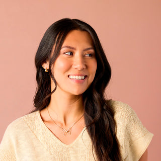 Woman with long dark hair wearing a beige sweater against a beige background