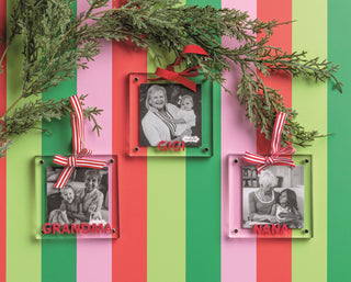 Three square acrylic photo frame ornaments labeled "GRANDMA," "GIGI," and "NANA" in red lettering, hanging from green pine branches.