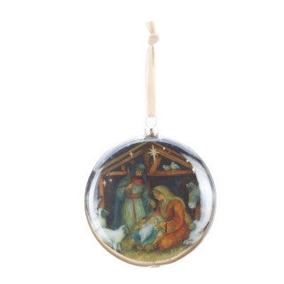 A round glass Christmas ornament featuring a colorful painted nativity scene with Mary, Joseph, baby Jesus, and a star, suspended by a cream-colored hanging ribbon against a white background.