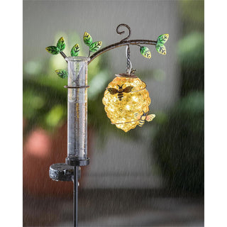Solar-powered rain gauge with decorative light and leaf design on a blurred background