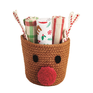 Crocheted reindeer basket with Christmas-themed towels and straws on a white background