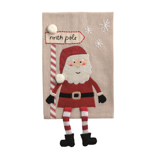 Decorative wall hanging with a cartoon Santa Claus holding a candy cane and 'North Pole' sign on a beige background.