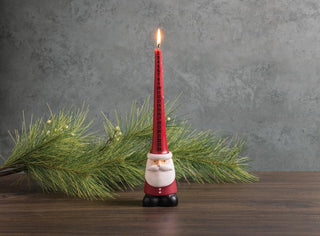 Red count down candle with Santa Claus design on a wooden surface with greenery