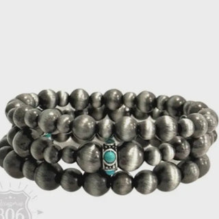 Stack of silver beaded bracelets with a turquoise accent 