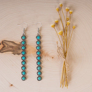 Turquoise beaded earrings on a wooden surface with dried flowers.