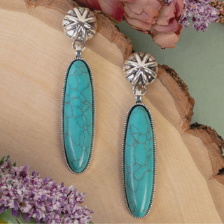 Silver drop earrings featuring sunburst-patterned studs and long, oval turquoise stones with natural marbling.