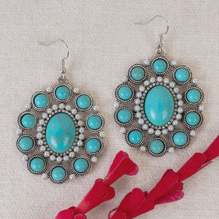 A pair of round silver-tone drop earrings featuring a large oval turquoise center stone, accented by a ring of small white pearls and an outer halo of round turquoise cabochons.