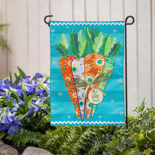 Decorative garden flag with carrots and flowers on a stand in front of a white fence.