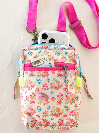 Floral-patterned crossbody bag with pink strap and phone pocket on a white background