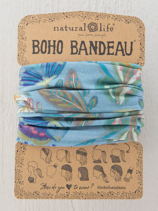 A Natural Life "Boho Bandeau" featuring a blue floral and leaf pattern, packaged on a brown cardboard backing. The display includes twelve small illustrations showing various ways to wear the versatile accessory, such as a headband, neck scarf, or wristband.