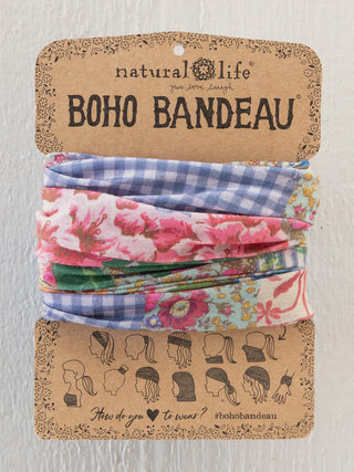
A Natural Life "Boho Bandeau" featuring a patchwork design of blue gingham and pink floral patterns. It is displayed on a brown cardboard backing that includes twelve illustrations of different ways to wear the accessory.