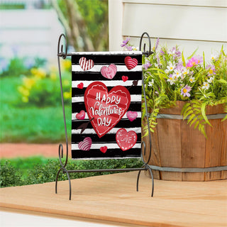 Decorative sign with 'Happy Valentine's Day' on a stand next to a wooden planter with flowers outdoors.