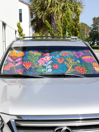 A colorful floral car windshield sun shade with a vibrant Mexican-inspired print, shown installed on the windshield of a silver vehicle outdoors.