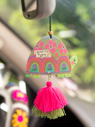 Colorful turtle-themed car mirror hanging with tassel against a blurred green background