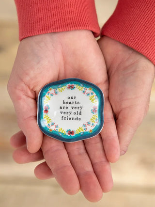 Small decorative tin held in hands with floral design and text on a beige background
