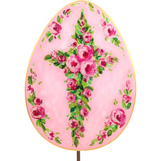 A large, egg-shaped decoration with a pink background, featuring a painted cross made of pink roses and green leaves, outlined with a gold border.
