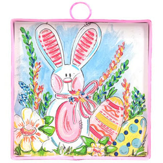 A square decorative plaque with a pink frame, featuring a painted illustration of a white Easter bunny holding a pink egg, surrounded by colorful flowers and decorated Easter eggs.