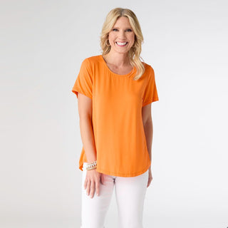 Woman wearing an orange t-shirt and white pants on a plain background