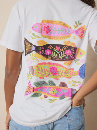 Person wearing a white t-shirt with colorful fish designs on a beige background