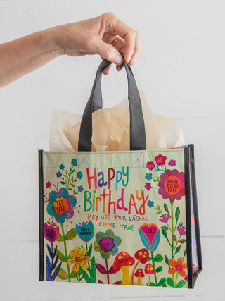 Hand holding a colorful 'Happy Birthday' bag with floral designs on a white background