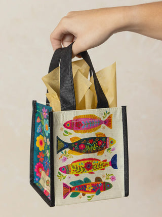 Colorful gift bag with fish design held by a hand against a beige background