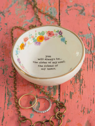 Decorative jewelry dish with floral design and text on a rustic wooden surface