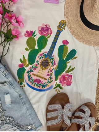 White shirt with guitar and cactus design, straw hat, denim shorts, sandals, and pink flowers.