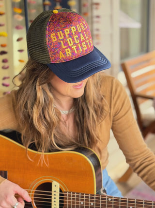 Person playing guitar wearing a cap with 'Support Local Artists' text