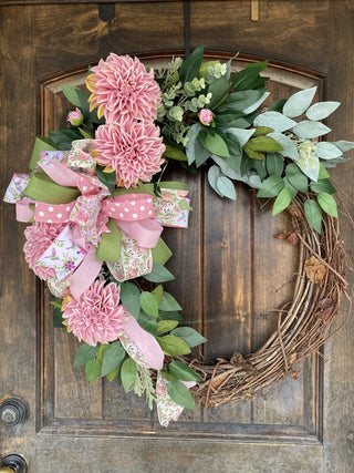 Floral grapevine wreath with pink flowers and green leaves on a wooden door