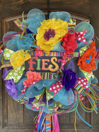 Colorful 'FIESTA' sign and  wreath with flowers and ribbons on a light blue mesh base on a wooden door.