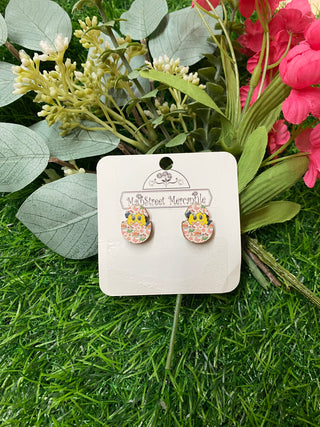 Pair of floral easter egg earrings with a chick peeking out on a card with greenery in the background