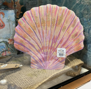 A decorative seashell-shaped wall piece painted in pink, peach, and purple tones with glittery gold accents