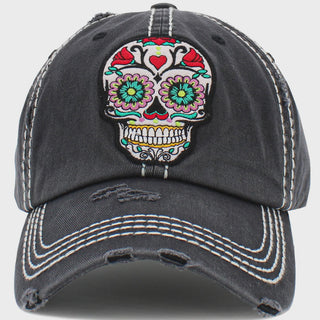 A distressed black baseball cap featuring a colorful embroidered sugar skull patch on the front, with white contrast stitching and distressed details on the brim.