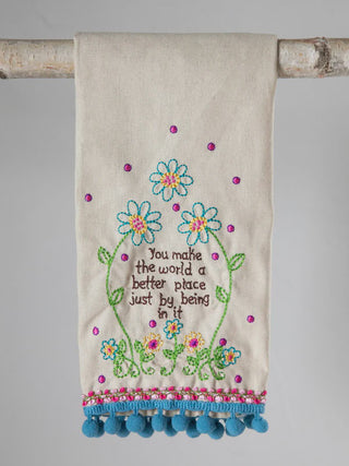 Embroidered towel with floral design and text on a wooden stick against a gray background