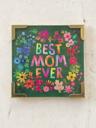 Framed artwork with 'Best Mom Ever' text surrounded by colorful flowers on a white wall.