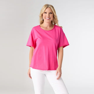 Woman wearing a bright pink top and white pants on a gray background