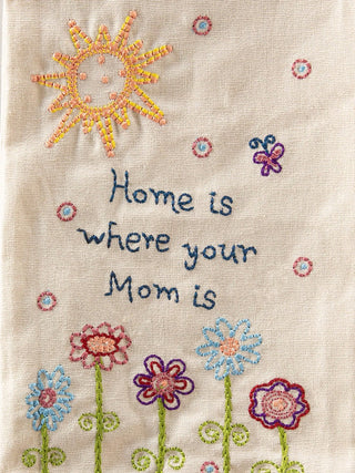 Embroidered text 'Home is where your Mom is' with flowers and a sun on a beige towel