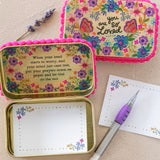 A set of floral tin notebooks and a matching floral pouch, shown open and closed on a white background with a purple pen nearby.