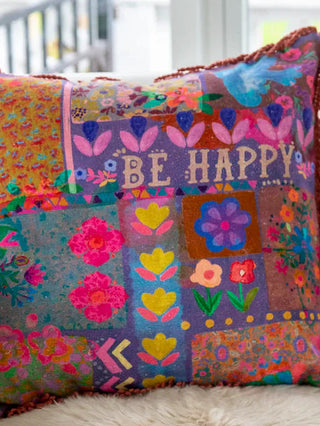 Colorful patchwork pillow with floral patterns and 'BE HAPPY' text on a white couch.