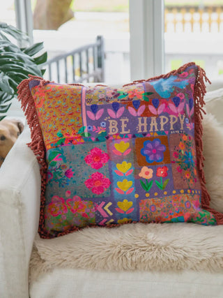 Colorful patchwork pillow with floral patterns and 'BE HAPPY' text on a white couch.