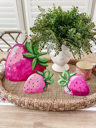 Decorative pink strawberry-shaped objects on a woven tray with a plant in the background.