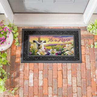 Decorative mat with 'He is Risen' text and floral design on a brick surface.