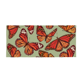 A rectangular fabric item, likely a beach towel or blanket, featuring a repeating pattern of orange and red monarch butterflies on a muted sage green background.