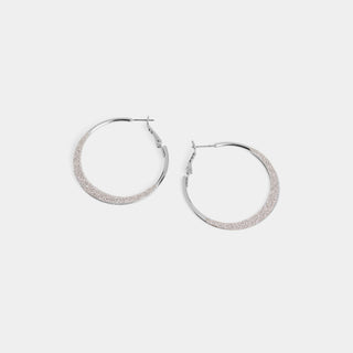 A pair of large round hoop earrings with a smooth silver polished inner frame and a wide glitter-textured front face, shown with a latch-back post closure.