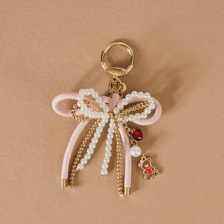 Keychain with pink ribbon, pearls, gold accents, and heart-shaped charms on a beige background