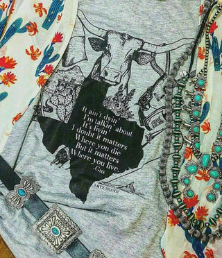 Gray t-shirt with black graphic and text, surrounded by colorful fabric and jewelry.