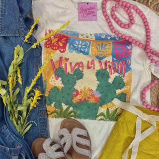 Colorful 'Viva La Vida' shirt with cactus design, denim jacket, sandals, and pink beads.